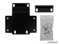 The Honda Pioneer 1000 Winch Mounting Plate kit, featuring a black metal plate with six holes, a smaller two-hole bracket, and a sealed bag of silver bolts and nuts, is displayed on a white background with the SuperATV logo in the bottom right corner.
