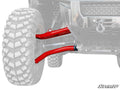 Close-up of the Honda Pioneer 1000 Atlas Pro 1.5 Forward Offset A-Arms, shown in red on an off-road vehicle. The rugged tire tread stands out, while the SuperATV logo appears in the corner and the rest of the vehicle is faded for emphasis.