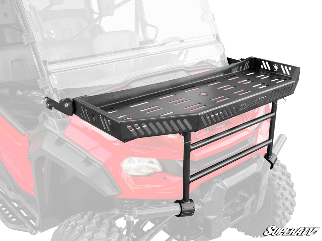 A Honda Pioneer 1000-6 Hood Rack Charlie is mounted to the front of a red off-road vehicle. The black metal rack features side cutouts, a slotted base, two horizontal bars, and displays the SuperATV logo at the bottom right. The vehicle is partially faded