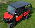 A Honda Pioneer 1000 with a tinted roof and mesh doors is parked on grass. A person in dark clothing and shorts sits inside, holding the steering wheel. The photo is taken from above at an angle.