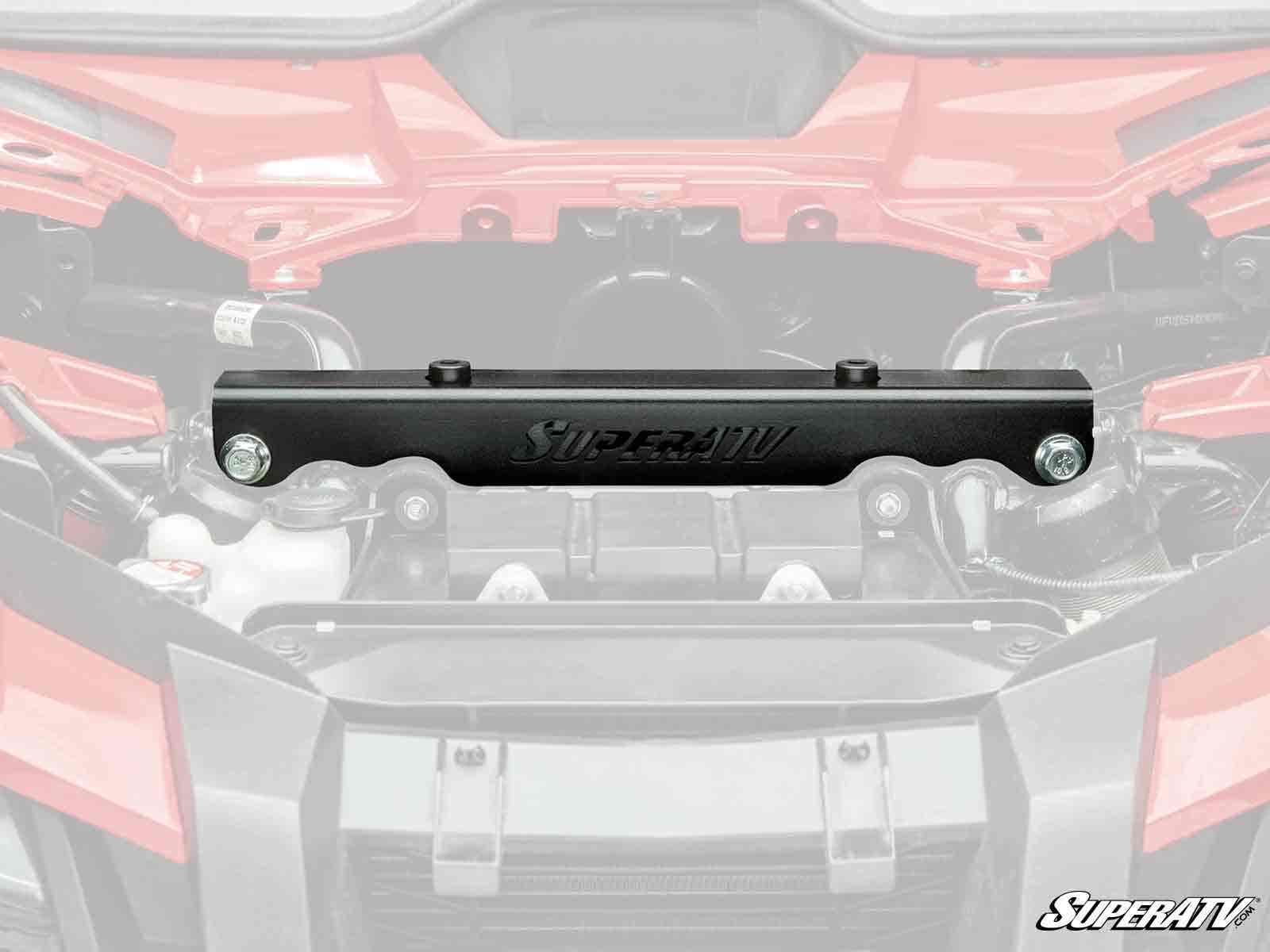 A black metal Honda Talon 1000 Front-End Brace Kit is shown centered against a faded off-road vehicle engine bay background. The bracket features two bolts on each end, and the SuperATV logo is visible in the bottom right corner.