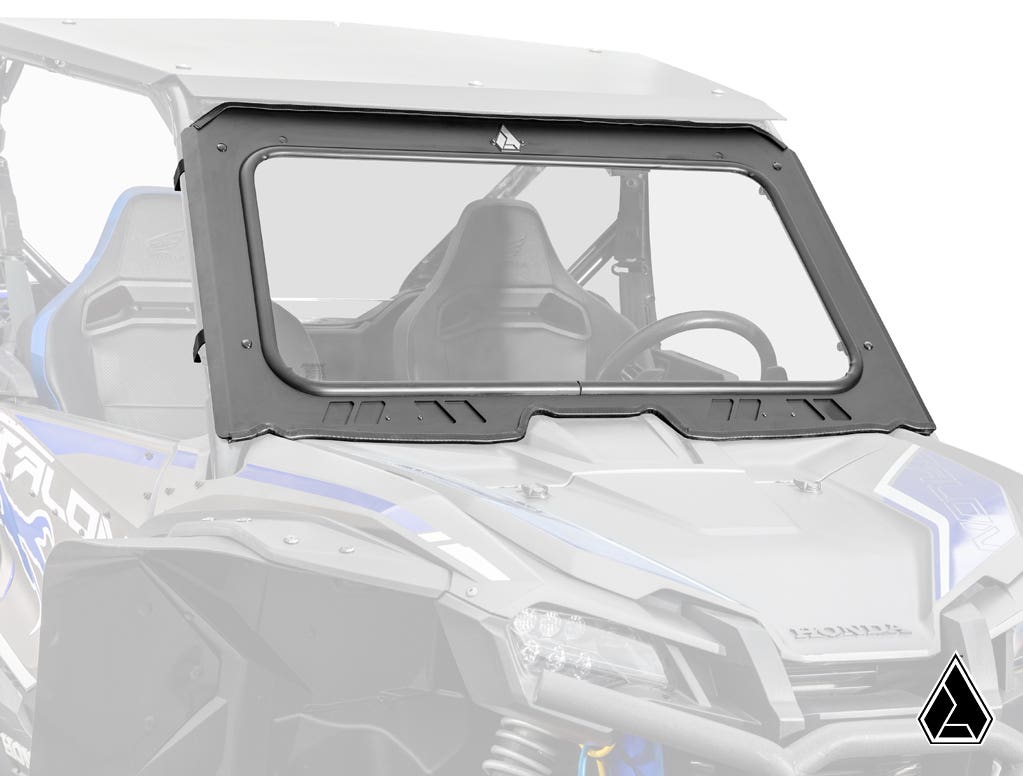 An Assault Industries Honda Talon 1000 Glass Windshield with a thick black frame and bottom cutout is installed on a blue and gray Honda side-by-side, mounted above the dashboard and steering wheel, with the logo in the lower right corner.