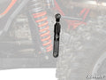 A close-up of a Honda Talon 1000 Sway Bar Shock shows a red coil spring, black shock absorber, and off-road tire. The black sway bar link is in focus with the SuperATV logo at the bottom right. Background components are faded.