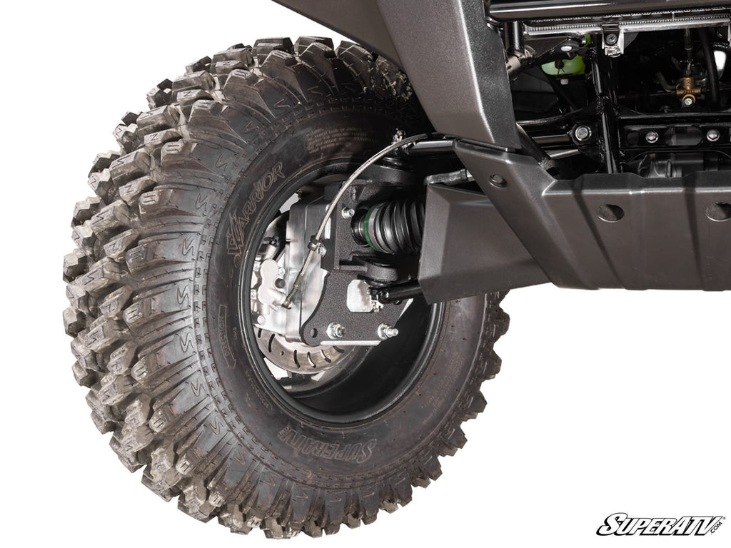 Close-up of a rugged Kawasaki Brute Force 4 Portal Gear Lift tire with deep tread, mounted on a black alloy wheel. Visible are the suspension system, brake disc, undercarriage, and a “SuperATV” logo in the corner.