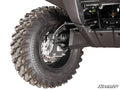 Close-up of a rugged Kawasaki Brute Force 4 Portal Gear Lift tire with deep tread, mounted on a black alloy wheel. Visible are the suspension system, brake disc, undercarriage, and a “SuperATV” logo in the corner.