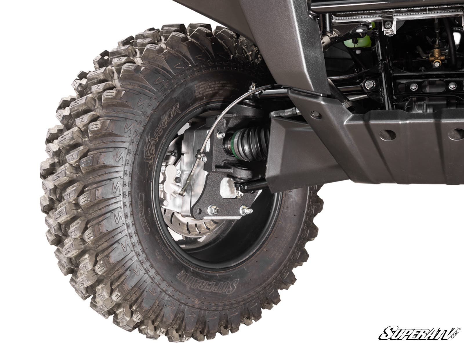 Close-up of a rugged Kawasaki Brute Force 4 Portal Gear Lift tire with deep tread, mounted on a black alloy wheel. Visible are the suspension system, brake disc, undercarriage, and a “SuperATV” logo in the corner.