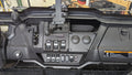 Dashboard of a Honda Pioneer 1000 (2022-2024) with an Ice Crusher Cab Heater, showing gear levers, control switches, toggle switches, circular dials, a warning label, and a device mount above the steering controls; workshop shelves/tools in background.