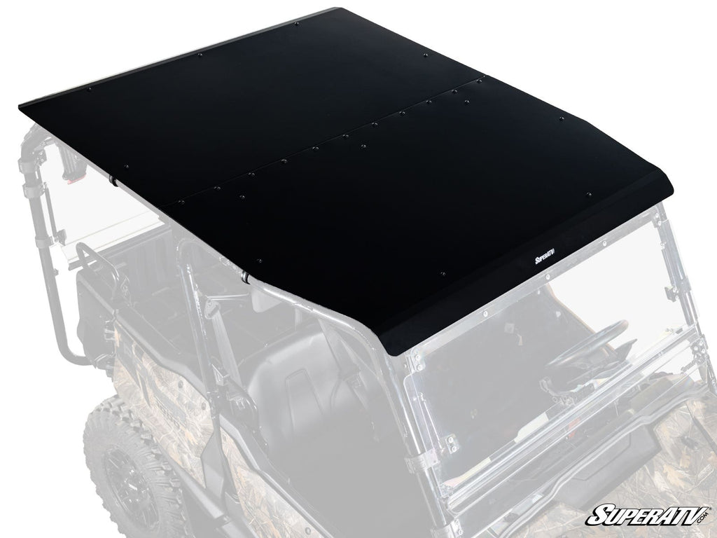 A matte black Honda Pioneer 1000-5 Aluminum Roof with exposed edge and center bolts is mounted on a camo UTV with a partial roll cage. The SuperATV logo appears at the front and bottom right corner of the rectangular metal roof.