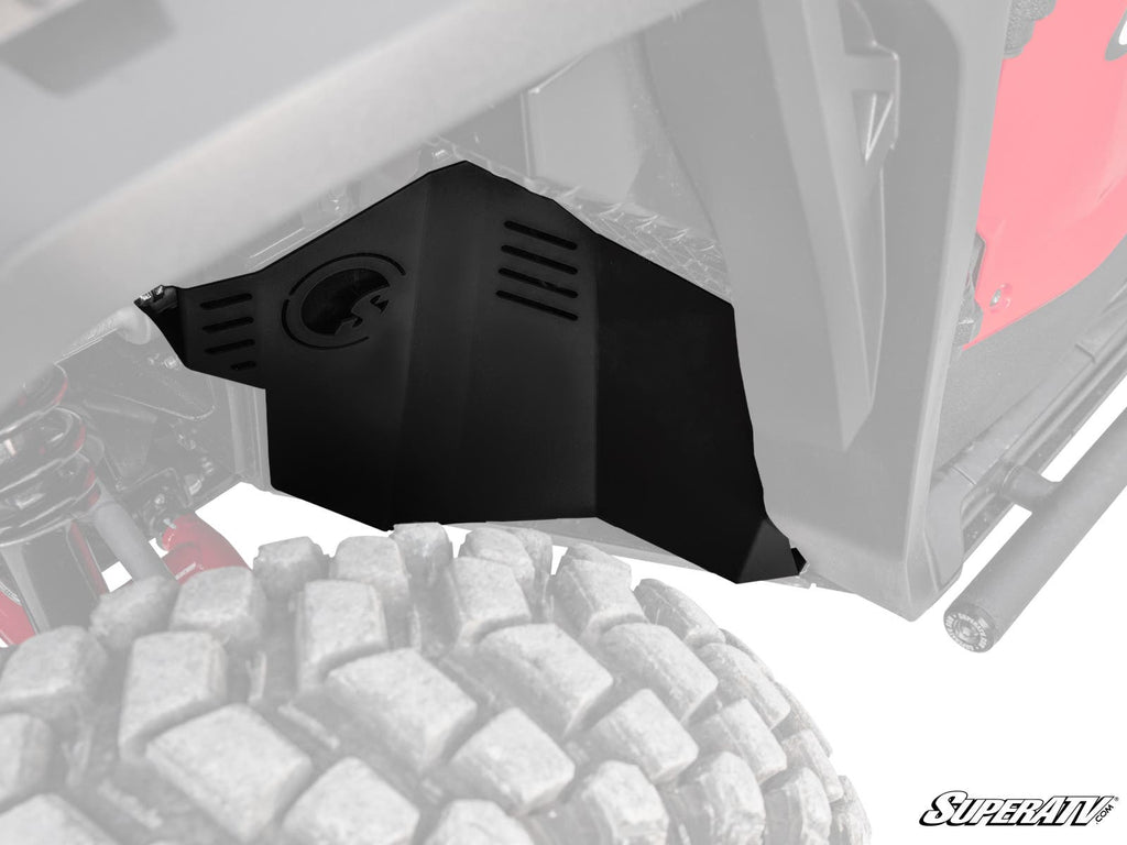 Close-up of Honda Pioneer 1000 Inner Fender Guards with vent-like slits, contoured to fit above the rugged off-road tire. Black plastic guard, part of red vehicle body and suspension visible. SuperATV logo in the corner.