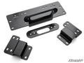 Four black metal brackets of different shapes and sizes, each with multiple bolt holes, are arranged on a white background. They have smooth, shiny surfaces. The SuperATV logo is in the bottom right. Product: Honda Pioneer 500 Winch Mounting Plate.