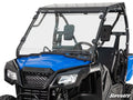 A close-up of a blue Honda side-by-side with a Honda Pioneer 500 Full Windshield, black framework, padded headrest, roll cage, steering wheel, open seating, and “SuperATV” branding in the lower right corner.