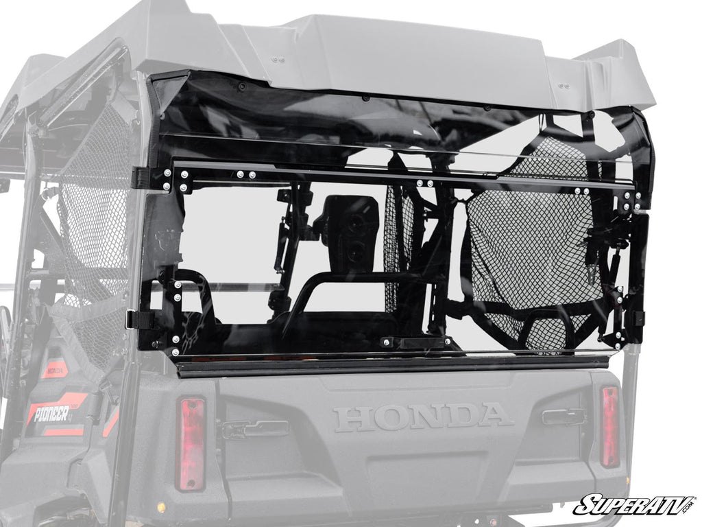 Close-up of a Honda Pioneer 700-4 Rear Windshield by SuperATV, featuring a black mesh window panel with metal framing and attachment hardware. The partially transparent panel offers a view into the vehicle’s interior, with SuperATV branding visible.