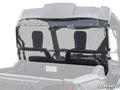 A clear Honda Pioneer 700 Rear Windshield is installed on a gray Honda utility vehicle, covering the space behind the two headrests and secured with black fasteners. The truck bed, roll cage, and SuperATV logo in the lower right are visible.