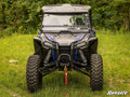 A Honda Talon 1000 equipped with a Winch Mounting Plate is parked on grass in front of a forest. It features large rugged tires, visible suspension, and a red tow strap on the front bumper. “SuperATV” logo appears in the lower right corner.