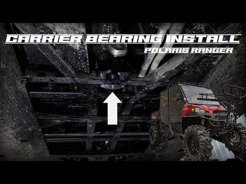 A view under a Polaris Ranger shows the drive shaft and a large white arrow pointing upward to the Polaris Ranger Heavy-Duty Carrier Bearing. Text reads Carrier Bearing Install Polaris Ranger. A red UTV appears in the bottom right corner.