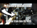 Close-up of an Assault Industries Heavy Duty Turret Rear Sway Bar End Link (Fits: Can-Am Maverick X3), with a large arrow pointing at the metal part. White bold text on image: Fixed A Weak Link On Our Can-Am Maverick X3. Automotive parts and tubing visibl