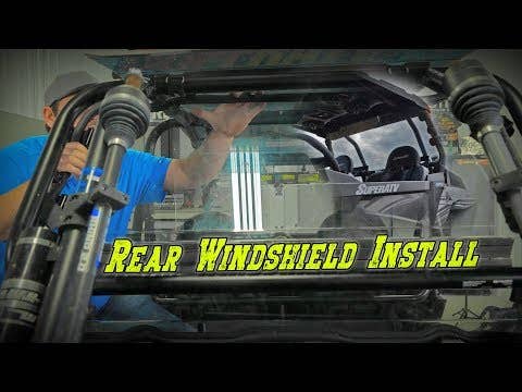 A person in a blue shirt installs a Polaris RZR XP Turbo Rear Windshield on an off-road vehicle inside a garage. Bold yellow text, “Rear Windshield Install,” spans the lower part of the image.