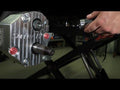 A close-up shows a person’s hand using a power tool on a Polaris RZR XP 1000 4 Portal Gear Lift. The cylindrical part extends from the gear lift, which is mounted on a black frame in a workshop setting.