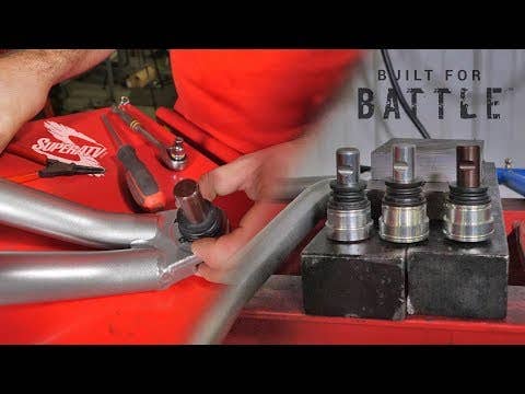 A person installs a Polaris Ranger XP 800 Ball Joint into a silver suspension arm on a red workbench with tools. Three Polaris Ranger XP 800 Ball Joints stand upright on a block at right, beneath the words “BUILT FOR BATTLE.”.