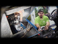A man in a green shirt and black cap sits by an off-road vehicle, holding a Can-Am Maverick X3 Heavy-Duty Carrier Bearing. An inset close-up shows him installing the bearing inside, focusing on mechanical components and bolts. Trees and workshop tools are