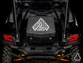 A rear view of a black Kawasaki Teryx KRX 1000 shows the Assault Industries Cooler/Cargo Box, featuring a white geometric logo and secured on the cargo bed. Red tail lights, rugged tires, and protective bars highlight the vehicle’s robust design.