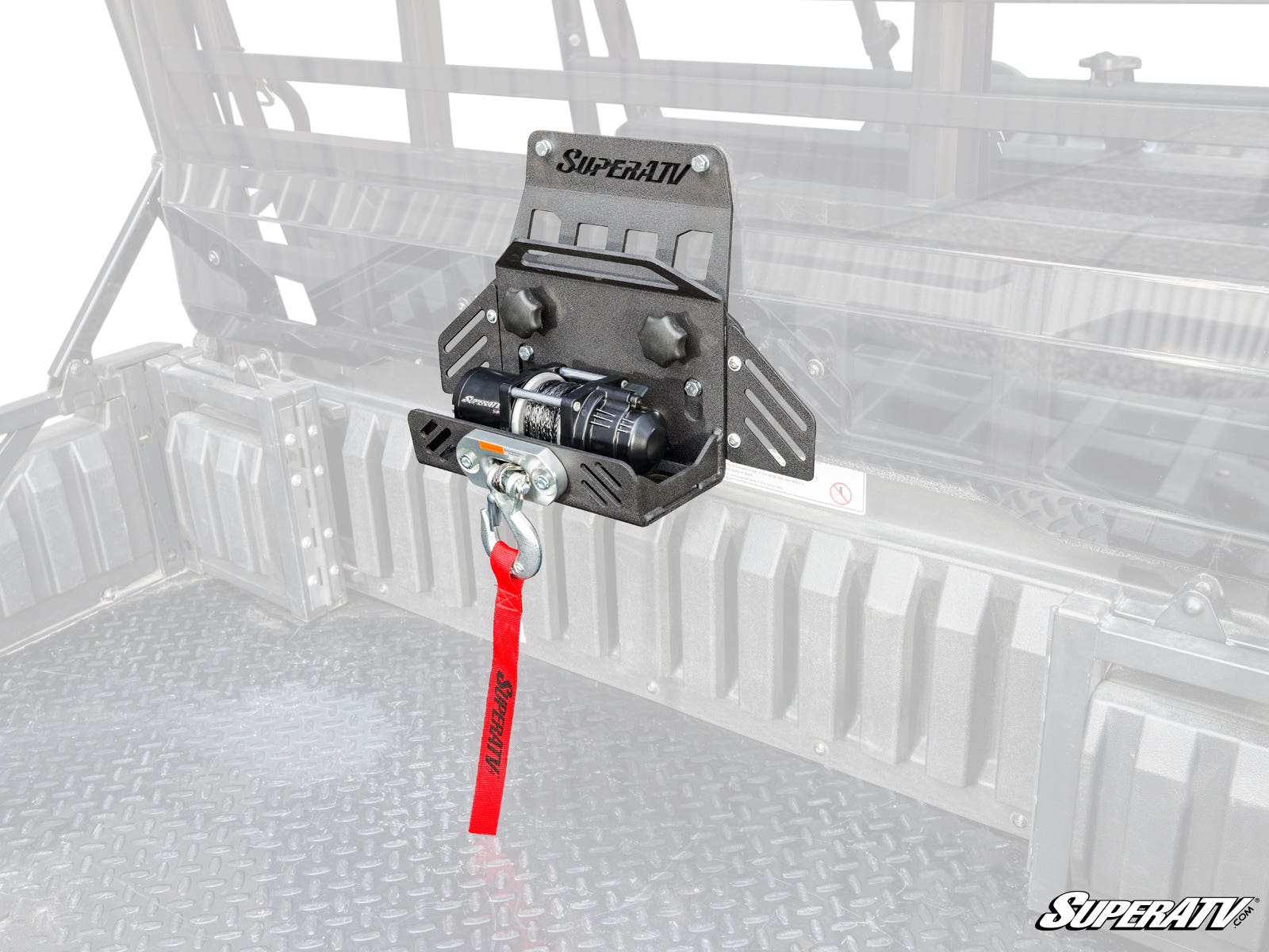 A Kawasaki Mule Pro Bed Winch with a small winch and red strap is mounted to the front interior of a rugged metal cargo bed in a utility vehicle, with the faded background emphasizing the winch mount and winch in front.