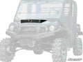 The Kawasaki Mule Pro Hood Scoop is shown from the front at a slight angle on a rugged off-road utility vehicle with large knobby tires, tall ground clearance, protective windshield, and the SuperATV logo in the bottom right corner.