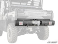 Close-up of a Kawasaki Mule Pro with a Kawasaki Mule Pro Winch Ready Rear Bumper by SuperATV, featuring two D-ring shackles, a center-mounted winch, large rugged tires, and a cargo bed. SuperATV logo appears in the corner.
