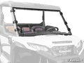 A Kawasaki Ridge Full Windshield with black clamps is mounted on a white Kawasaki utility vehicle. The full-front windshield, held by visible brackets, reveals two seats with headrests and a steering wheel behind the glass.