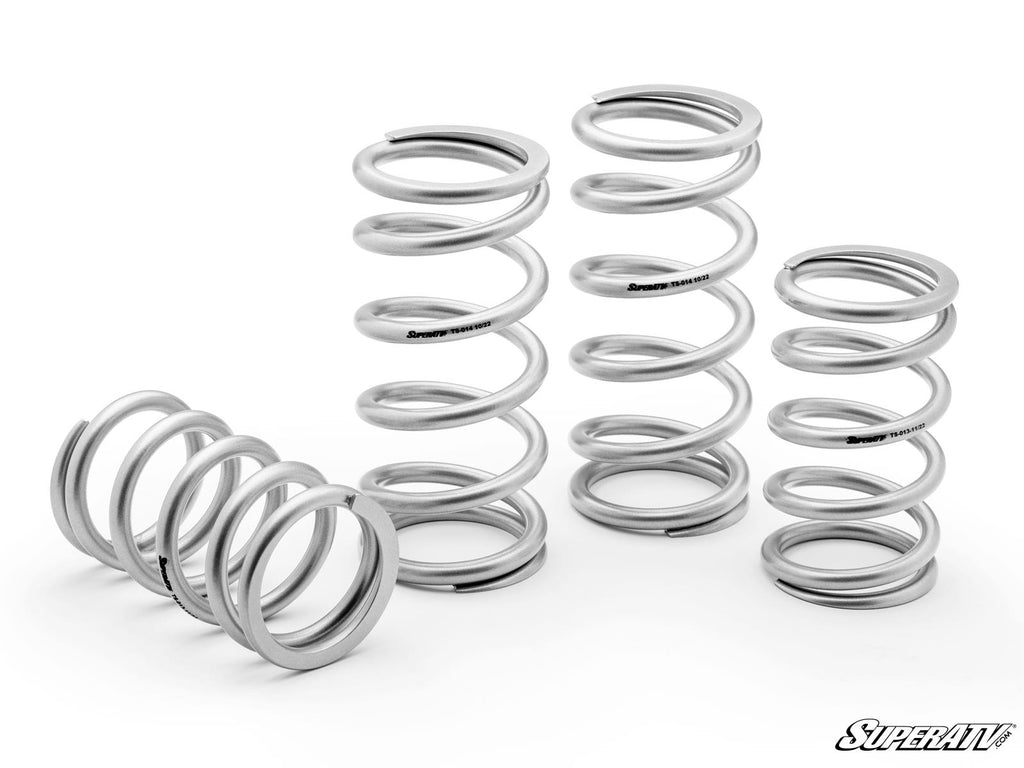 Four new, shiny metallic springs of different sizes from the Kawasaki Teryx KRX 1000 Tender Spring Kit are arranged on a white background. Three stand upright, one lies down. The SuperATV logo appears in black at the lower right corner.