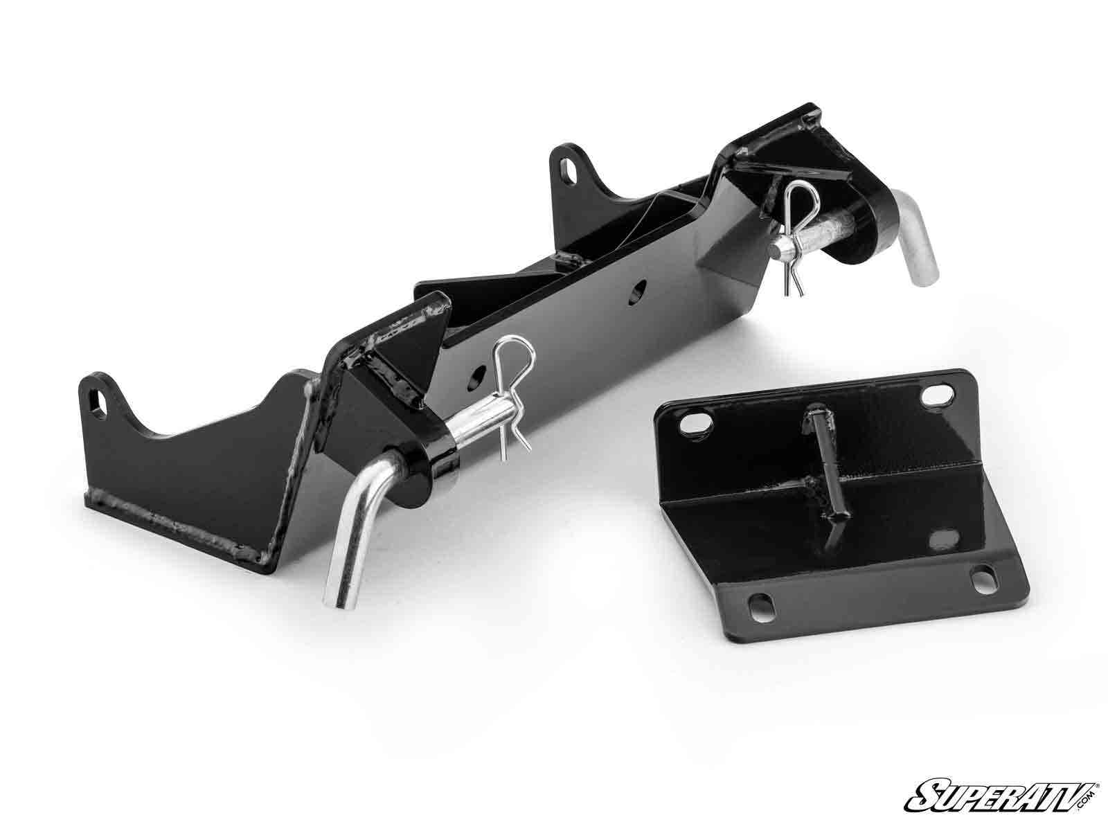 The Kawasaki Teryx Plow Pro Snow Plow Mount kit includes a black metal main bracket, mounting plate, two hitch pins, and cotter clips with a glossy finish and angled design, shown on a white background with the SuperATV logo in the corner.