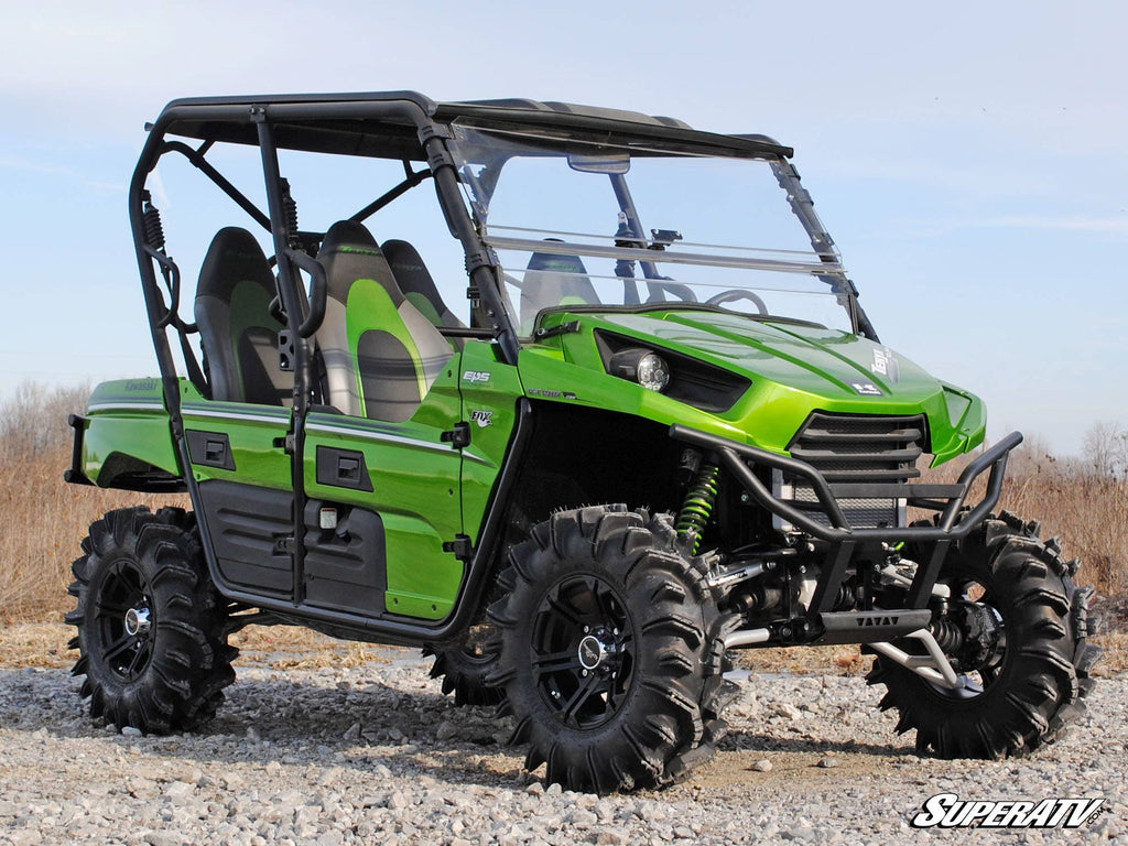 A Kawasaki Teryx with High Clearance 1.5 Forward Offset A-Arms is parked on rocky terrain, featuring four seats, rugged tires, a roll cage, windshield, black roof, and prominent suspension; SuperATV branding is at the bottom right.