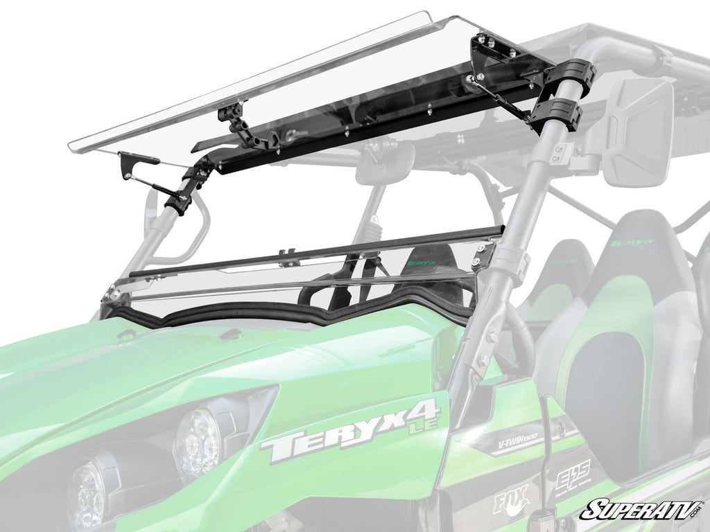 A Kawasaki Teryx S Flip Windshield, shown partially open on a green Teryx4 off-road vehicle, is attached to the roll cage with black brackets. Two bucket seats and the vehicles logo are visible against a white background.