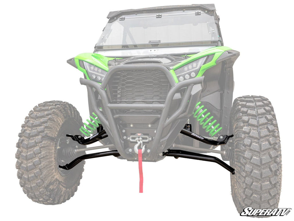 Front view of Kawasaki Teryx KRX High Clearance 1.5 Forward Offset A-Arms with green and black bumper, large rugged tires, bright green suspension springs, and a visible winch with red strap; background faded to spotlight the front suspension.