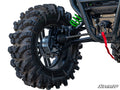 Close-up of a Kawasaki Teryx KRX 1000 4 Portal Gear Lift installed, showing rear suspension, green springs, black shock absorbers, large rugged tire with deep treads, suspension arms, and winch cable. Kawasaki and SuperATV logos are visible on a white bac