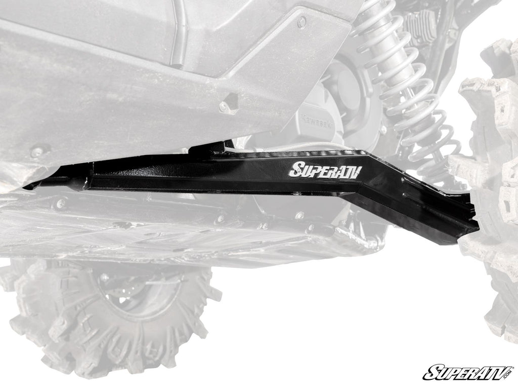 A close-up of black metal Kawasaki Teryx KRX 1000 High-Clearance Rear Trailing Arms installed on an off-road vehicle with large treaded tires and visible suspension; the arms are highlighted while the vehicle appears partially faded.