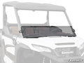 A Kawasaki Ridge Half Windshield is installed on a white Kawasaki side-by-side utility vehicle, covering the lower front and secured with two black brackets. The SuperATV logo is displayed in the bottom right corner.