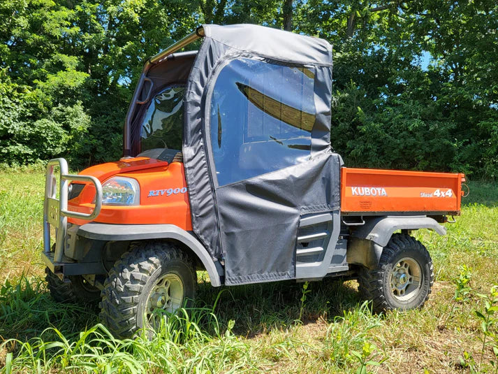 A bright orange Kubota RTV900 utility vehicle, equipped with the Kubota RTV Soft Door Kit for all single cab models, features a silver fabric-sided cab enclosure, large off-road tires, and is parked on grass with green trees in the background.