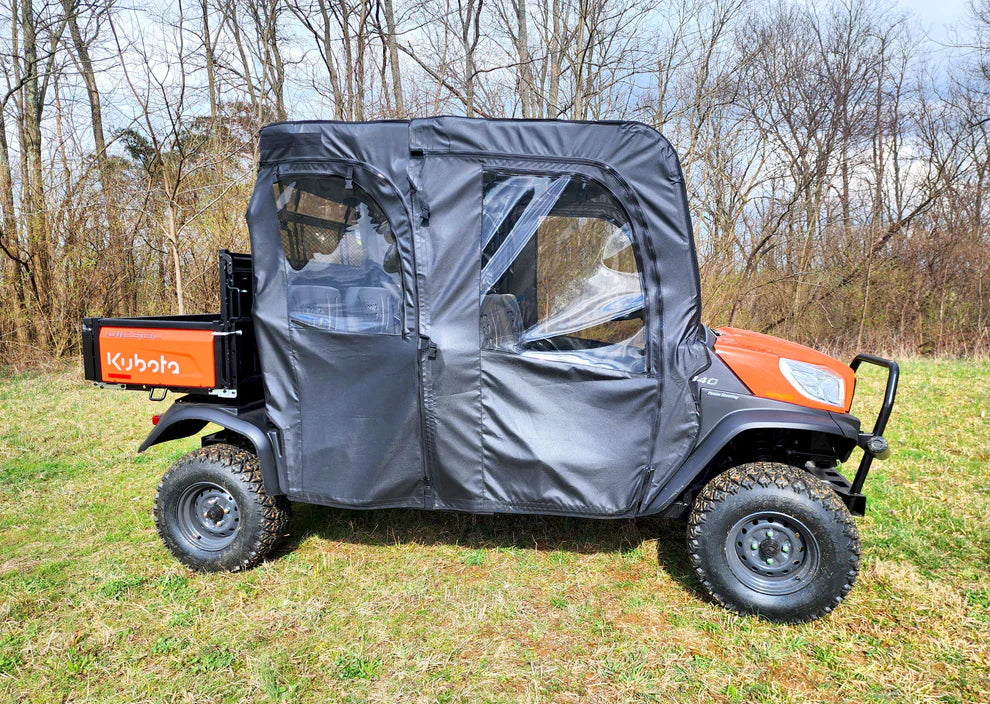 A Kubota RTV X1140 with the Door/Rear Window Combo, featuring a black canvas enclosure and clear plastic windows, is parked on grass. The orange and black utility vehicle has off-road tires, with leafless trees in the background.