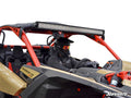 A person in a black helmet and goggles sits in the driver’s seat of a tan and red Can-Am Maverick X3 equipped with a large LED light bar mounted using the Can-Am Maverick X3 Light Bar Mounting Kit. The background is plain white.