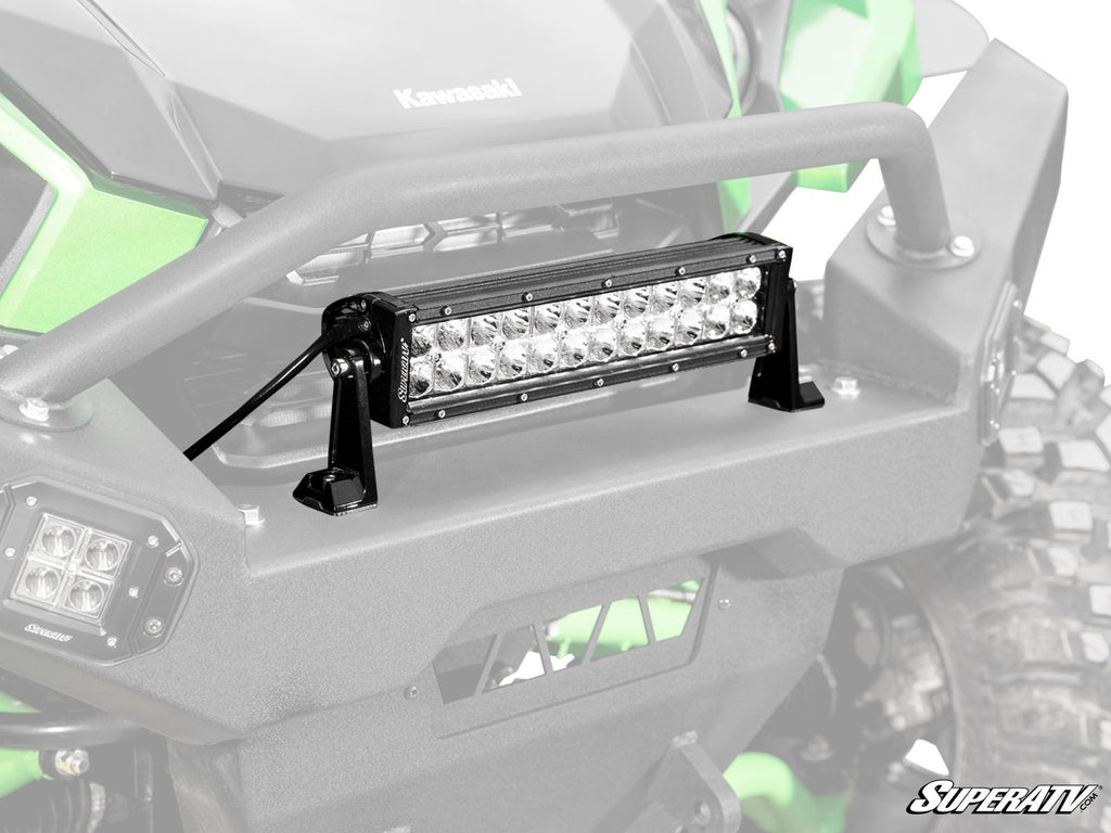 Close-up of a 12 LED Combination Spot / Flood Light Bar mounted on the front bumper of a green Kawasaki off-road vehicle, featuring multiple LEDs, black mounting brackets, and the SuperATV logo in the bottom right corner.