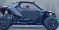 A man in a cap and brown jacket sits inside a matte black Can Am Maverick R fitted with the 2 Seat Door Set, featuring large rugged tires and parked on asphalt marked by a yellow line. The blurred background shows gray tones.