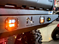 Close-up of the CanAm Defender Rear Bumper w/ light pods, featuring two square LED lights (one glowing orange), a cutout NL NO LIMIT logo, and large tires underneath—showcasing durability and custom styling.