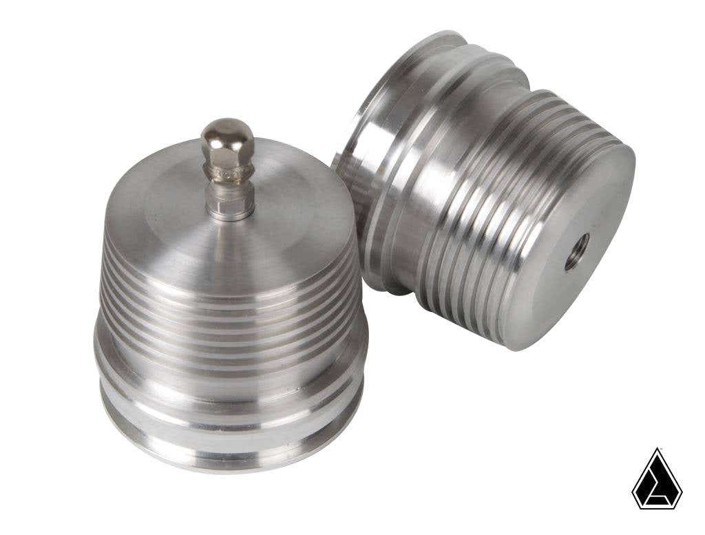 Two silver, cylindrical Assault Industries Shock Reservoir Nitrogen Expansion Caps (for Fox Shocks) are shown—one upright with a top knob, one on its side revealing an end hole. A small black triangular logo appears at the bottom right.