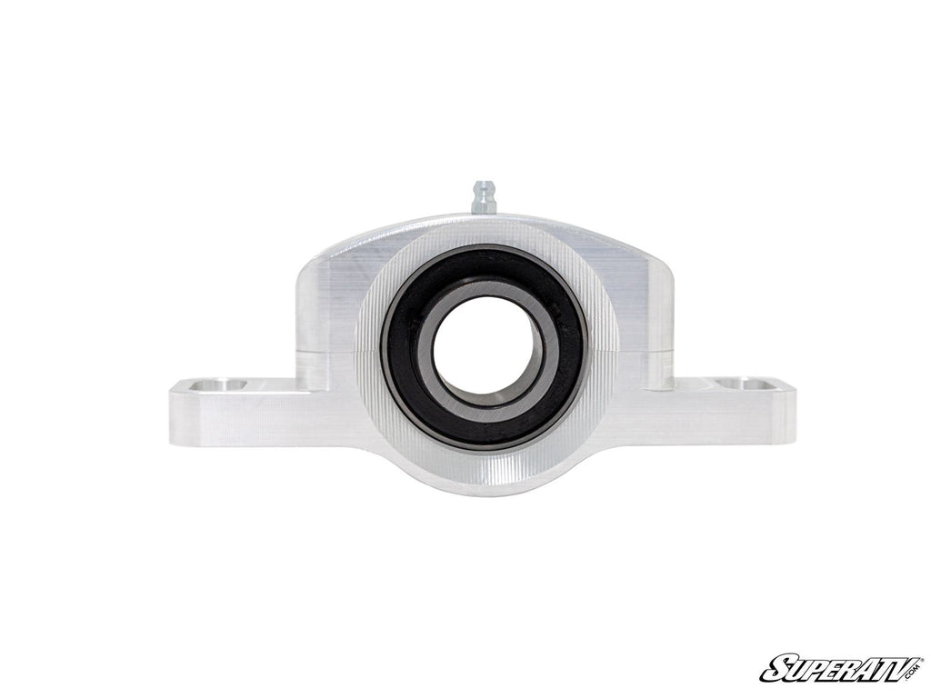 A front view of the SuperATV Carrier Bearing Rebuild Kit shows a silver, machined aluminum bearing carrier with a large central black bearing and two side extensions on a white background. The SuperATV logo is in the bottom right corner.
