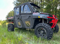 A Polaris Ranger Crew XP 1000 equipped with a Seizmik Framed Door Kit and rugged tires, featuring a red front bumper and Ranger branding, is parked on tall grass near trees and greenery.