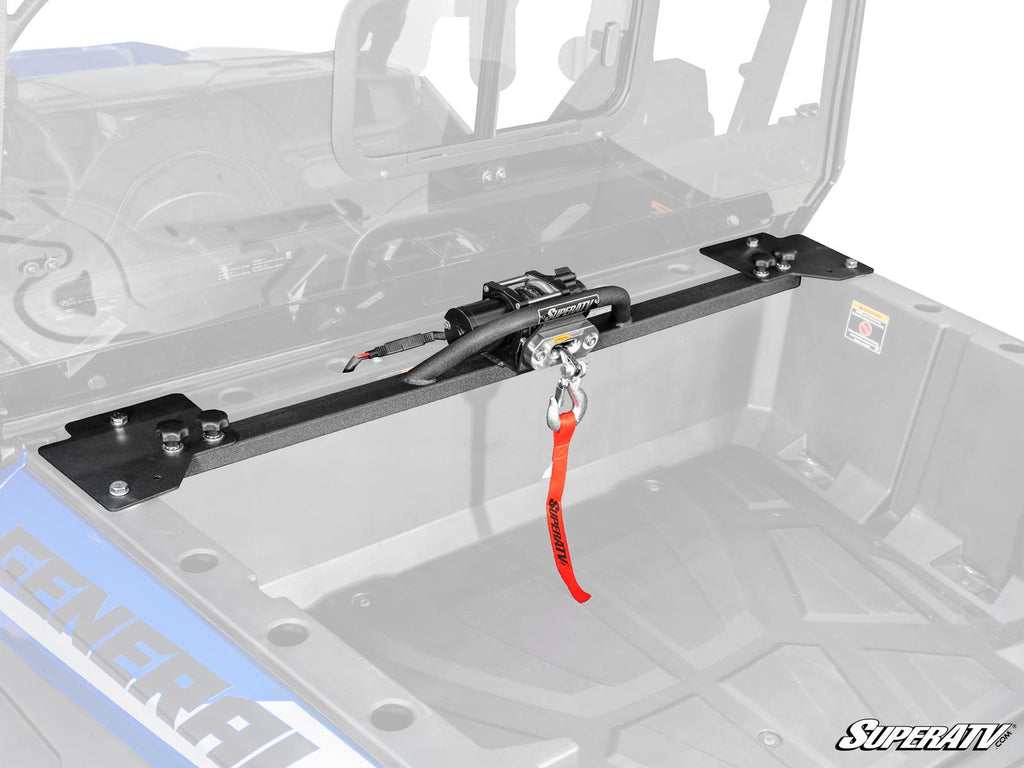 A Polaris General 1000 Bed Winch with a black metal mount and red strap is installed across the bed of a blue off-road vehicle. The empty bed and faded background highlight the secure mounted winch system.