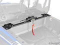 A Polaris General 1000 Bed Winch with a black metal mount and red strap is installed across the bed of a blue off-road vehicle. The empty bed and faded background highlight the secure mounted winch system.