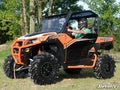 A rider in a helmet and green shirt drives an orange and black Polaris General with large tires on grassy terrain. Displayed is the Polaris General Front Leveling Kit. The SuperATV logo appears in the lower right corner against a backdrop of trees.