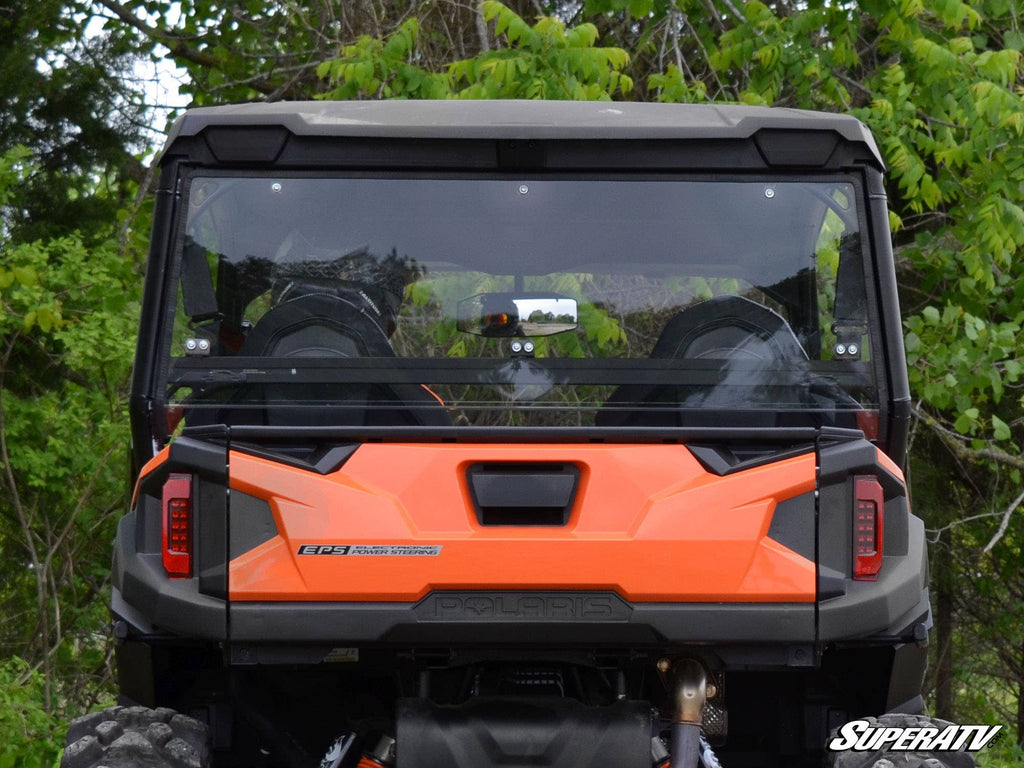 Rear view of a Polaris General XP 1000 with the SuperATV Rear Windshield, black roof, and two headrests. The vehicle is set among lush green trees. The SuperATV logo is visible in the bottom right corner.